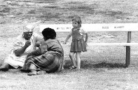 Black nannies sit on the grass looking after white children because the park bench is for whites